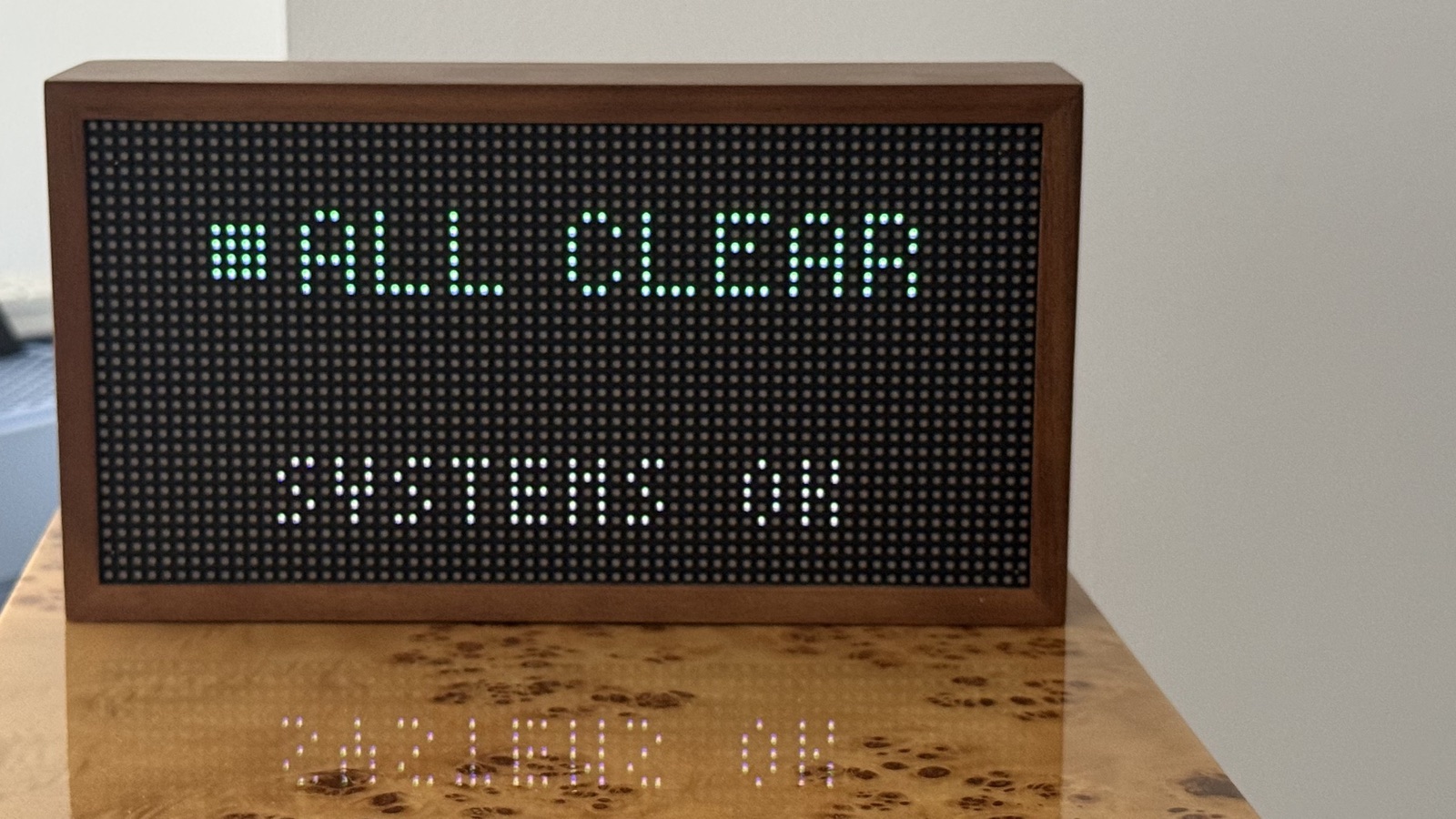 An original walnut Tidbyt display showing the TIDBYTS All Clear system state in a real room